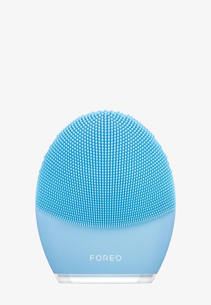 Silikonowy oczyszczacz do twarzy, okrągły kształt, jasnoniebieski kolor, teksturowana powierzchnia z małymi silikonowymi włoskami, przezroczysta podstawa z logo "FOREO".