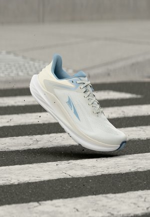 Chaussure de course blanche et bleu clair en l'air au-dessus d'un passage piéton zébré sur un trottoir en bitume.