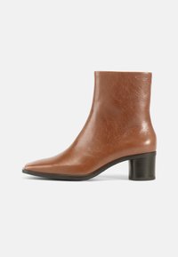 Ruskeat nahkaiset nilkkurit, joissa on terävä kärki, teksturoitu viimeistely ja keskikorkea palikkakorko. Yksinkertainen muotoilu ilman näkyviä metalliosia tai kuvioita.