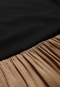 Close-up of brown pleated fabric joined to smooth black fabric, highlighting texture and seam detail.