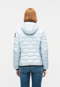 Άτομο με ίσια κόκκινα μαλλιά που φοράει ανοιχτό μπλε μπουφάν με κουκούλα και σκούρα μπλε τζιν, βλέποντας από πίσω.