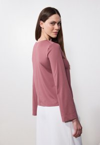 Top de manga larga en un suave tono rosa claro, fabricado con un tejido blando, que presenta un escote redondeado y un corte recto. La parte trasera tiene un detalle de costura.