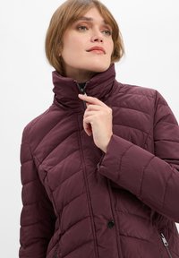 Bordeaux pufferjack met een hoge kraag, diagonaal quiltpatroon, ritssluiting en zijzakken. Gladde, glanzende textuur.