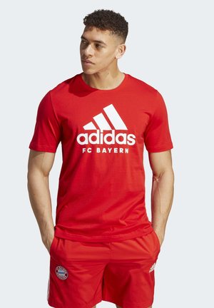 La camiseta roja de Adidas del FC Bayern presenta un logo blanco y tres franjas. Combinada con pantalones cortos rojos a juego, exhibe un look atlético clásico.