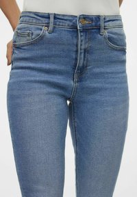 Modre denim hlače s prilegajočim dizajnom, petimi žepi, visokim pasom in subtilnim izbledenjem, z zlatimi kovinskimi dodatki in šivi.