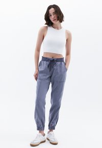 Grijze katoenen joggingbroek met elastische boorden en een trekkoord in de taille, gecombineerd met een witte geribbelde crop top en witte sneakers.