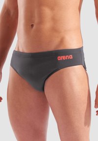 Czarne kąpielówki wykonane z elastycznej tkaniny o gładkiej fakturze. Posiadają wyrazisty pomarańczowy logo "arena" z boku oraz klasyczny krój.