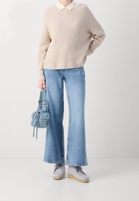 Beige gebreide trui met een witte blouse, lichtblauwe flared jeans, grijze suède schoenen en een kleine blauwe leren tas met accenten.