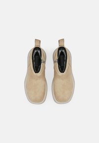 Beige mokka nilkkurit, joissa on musta vuori, sivuvetoketjulliset ja kontrastivärinen valkoinen kumipohja.