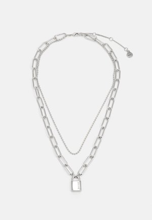 Sølvkjede med to lag: en stor lenke-kjede og et perlekjede, med en liten hengelås-pendant. Strukturert metallfinish.