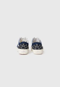 Blå og hvite mønstrede lerrets sneakers med hvite såler, med en strukturert design på baksiden og runde åpninger for snøringer.