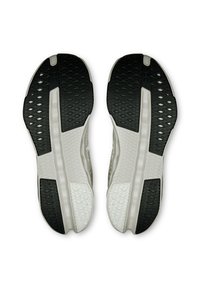 Schwarz-weißes Sohle eines Sportschuhs mit strukturiertem Gummi für Grip, einem glatten Mittelteil und einem hexagonalen Muster für Flexibilität.