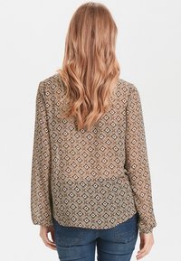 Långärmad blus i brunt med geometriskt mönster. Har en V-ringning och en rak passform. Tyget har en mjuk yta. Bärs med jeans.