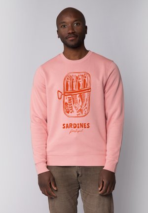 Sweatshirt rose avec un graphisme de boîte de sardines orange et le texte « SARDINES Portugal ». Fabriqué en tissu doux, il a un col rond et des poignets côtelés.