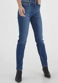 Jeans ajustados en denim azul oscuro, con un diseño clásico de cinco bolsillos, un ligero desgaste y una cremallera con cierre de botón.