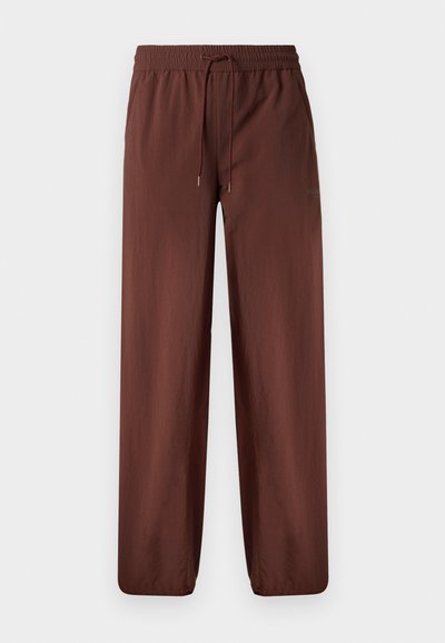 Brūni, viegli bikses ar elastīgu jostasvietu, ar auklu detaļu un sašaurinātām kājām. Gluda tekstūra, bez kabatām, minimāla zīmola identifikācija.