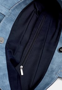 Sac en denim avec un extérieur bleu clair et une doublure intérieure bleu foncé, doté d'une poche zippée et d'une fermeture à bouton, structuré, avec une surface texturée.