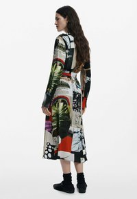 Robe longue présentant un collage d'imprimés, y compris des feuilles, des formes abstraites et du texte ; couleurs noir, rouge et vert ; taille cintrée avec une ceinture.