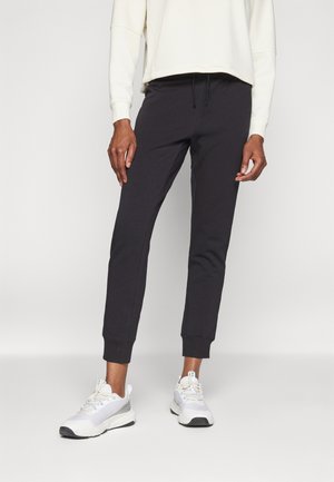 Pantalones de chándal negros de tela suave, con cintura ajustable con cordón y puños ceñidos, combinados con zapatillas deportivas blancas.