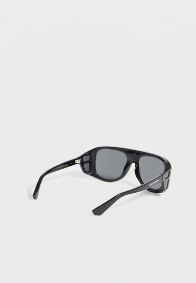 Μαύρα ορθογώνια γυαλιά ηλίου με σκούρους φακούς, χοντρές μπράτσες και το λογότυπο "Dolce & Gabbana" στο δεξί βραχίονα, σε λευκό φόντο.