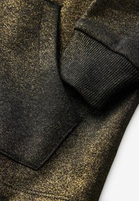 Sudadera negra con textura de purpurina dorada, presenta puños acanalados y un detalle de bolsillo diagonal. Tejido suave con un acabado brillante.