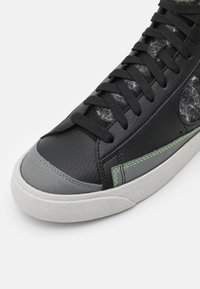Svart lädersneaker med grå detaljer, strukturerad yta, gröna sömnadsdetaljer och traditionellt snörningssystem. Gummisula synlig.