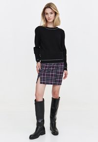Czarny sweter z długim rękawem z srebrnym akcentem na dekolcie, w połączeniu z mini spódniczką w kratę w kolorach fioletowym, kremowym i czarnym. Czarne kozaki za kolano.