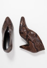 Brown heeled shoes with a snakeskin pattern, featuring a pointed toe and a cutout side. Made of textured material with a glossy finish.
