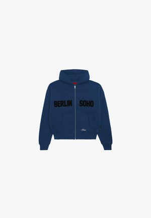 Marineblå hettejakke med glidelås og kengurulomme, med svart tekst "BERLIN" og "SOHO" på brystet, samt en liten logo ved kanten.