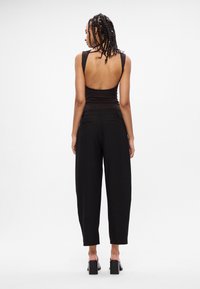 Crna bezrukavna majica s otvorenim leđima u kombinaciji s lako crnim hlačama. Odjeća ima glatku teksturu i suptilne detalje šivanja.