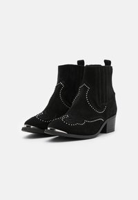 Botas de tobillo de ante negro con detalles de costura y acentos metálicos en la puntera. Cuenta con paneles laterales elásticos para un fácil calce. Diseño de tacón cuadrado.