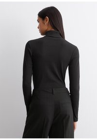 Schwarzer Rollkragenpullover mit langen Ärmeln, taillierter Schnitt, geripptem Material, kombiniert mit hoch taillierten Nadelstreifen-Hosen; minimalistischem Design und Farbschema.