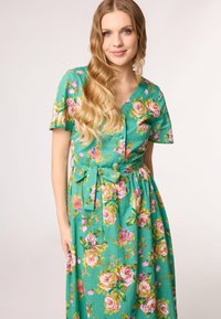 Blumenkleid im Maxistil mit grünem Hintergrund, kurzen Ärmeln, V-Ausschnitt und gebundenem Taillengürtel. Enthält rosa und gelbe Rosenmuster.