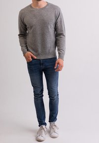 Maglione grigio chiaro in maglia con scollo rotondo, abbinato a jeans aderenti blu e sneaker bianche. Texture morbida e design semplice con polsini a costine.