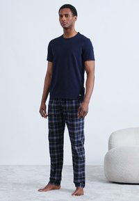 Tamsiai mėlynas medvilninis marškinėlis derinamas su languotomis medvilninėmis pižamos kelnėmis tamsiai mėlynos ir žalios spalvos atspalviais. Apranga pasižymi laisvu kirpimu ir elastine juosmens juosta.