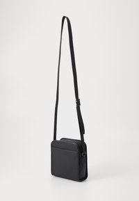 Black leather crossbody bag with a rectangular shape, adjustable strap, front zipper pocket, and smooth texture.