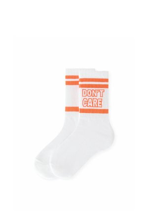 Paire de chaussettes blanches montantes avec des rayures orange et les mots "DON'T CARE" tricotés en orange sur la partie supérieure.