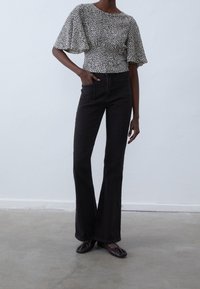 Černé rozšířené džíny spárované s tričkem s krátkým rukávem s vzorem, které má kulatý výstřih a texturovanou tkaninu. Obuv tvoří tmavé, zakulacené mokasíny.