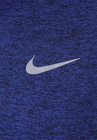 Nike-swoosh-logotyp i ljusgrått på en texturerad blå och svart tygbakgrund.