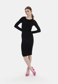 Svart långärmad figurnära klänning med rund halsringning. Matchad med klara rosa pumps med spetsig tå och dekorativ rosett.