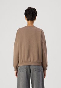 Sudadera marrón de corte holgado, con cuello redondo y puños acanalados. El material parece suave, con una textura lisa y un brillo sutil.