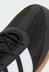 Sort sportsko med en mesh-overdel, suedepaneler og tre hvide striber. Kommer med sorte snørebånd og en gummirubber ydersål.