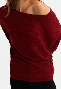 Pull bordeaux à encolure bardot en tissu côtelé avec une coupe ample et un tissu texturé. Il présente un ourlet incurvé et des détails froncés à la taille.