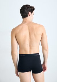 Boxeri din bumbac negru, cu un brâu elastic ce prezintă logo-ul "Calvin Klein" în roșu. Concepuți pentru un aspect mulat și confortabil.