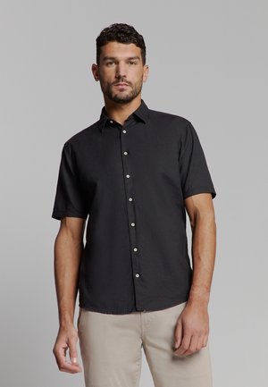Zwart kortemmers overhemd met knoopsluiting en kraag, een voorpand met knopen en witte knopen. De stof lijkt textuur te hebben. Gemaakt met lichte broek.