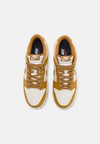 Nike sneakers med en hvid læderoverdel, brune detaljer og perforeret tåboks. Brune snørebånd og logo på tungen. Flad således design.