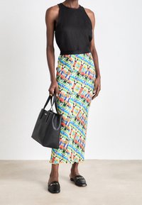 Top negro sin mangas, falda maxi con patrón colorido y dobladillo con forma de concha, bolso negro y mocasines deslizantes con detalle de cadena dorada.