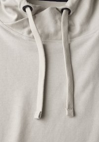 Sudadera con capucha de color gris claro, con una textura suave, que presenta cordones ajustables en color crema y detalles de costura mínimos.