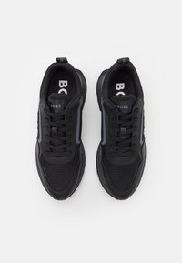 Une paire de sneakers BOSS noires avec des détails en mesh et en cuir, lacets noués et semelles intérieures griffées, présentée de dessus sur un fond blanc.