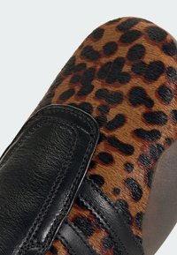 Topánky s leopardím vzorom s hladkým hnedým kožúškom a čiernymi koženými akcentmi, s suchým zipsom a elegantným zaobleným tvarom.